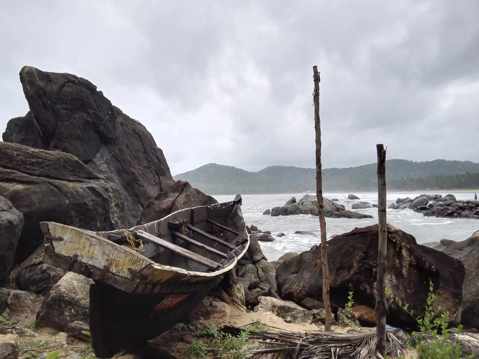Wrecked wooden boat against rocks on a stormy Goa beach